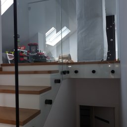 V-Glass - Szklana barierka z czarnymi elementami mocującymi, zabezpieczająca schody na poddaszu w Sokołowie Podlaskim, widok na zabawki dziecięce za szybą.