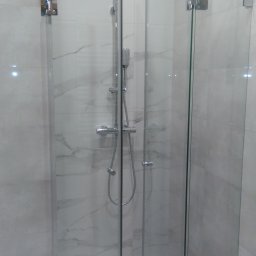 V-Glass - Szklana kabina prysznicowa z chromowanymi zawiasami i odpływem liniowym w posadzce, na tle marmurowych płytek.