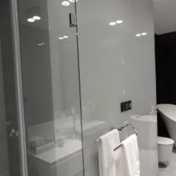 Nowoczesna łazienka z kabiną prysznicową ze szkła hartowanego, widoczny fragment umywalki, toaleta i wanna wolnostojąca, białe ręczniki na chromowanym wieszaku.