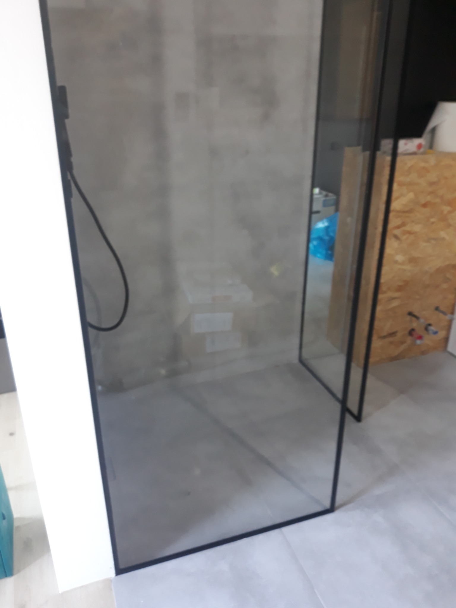 Nowoczesna kabina prysznicowa ze szklaną ścianą i czarnymi profilami, widoczna w trakcie montażu, z elementami instalacji w tle.