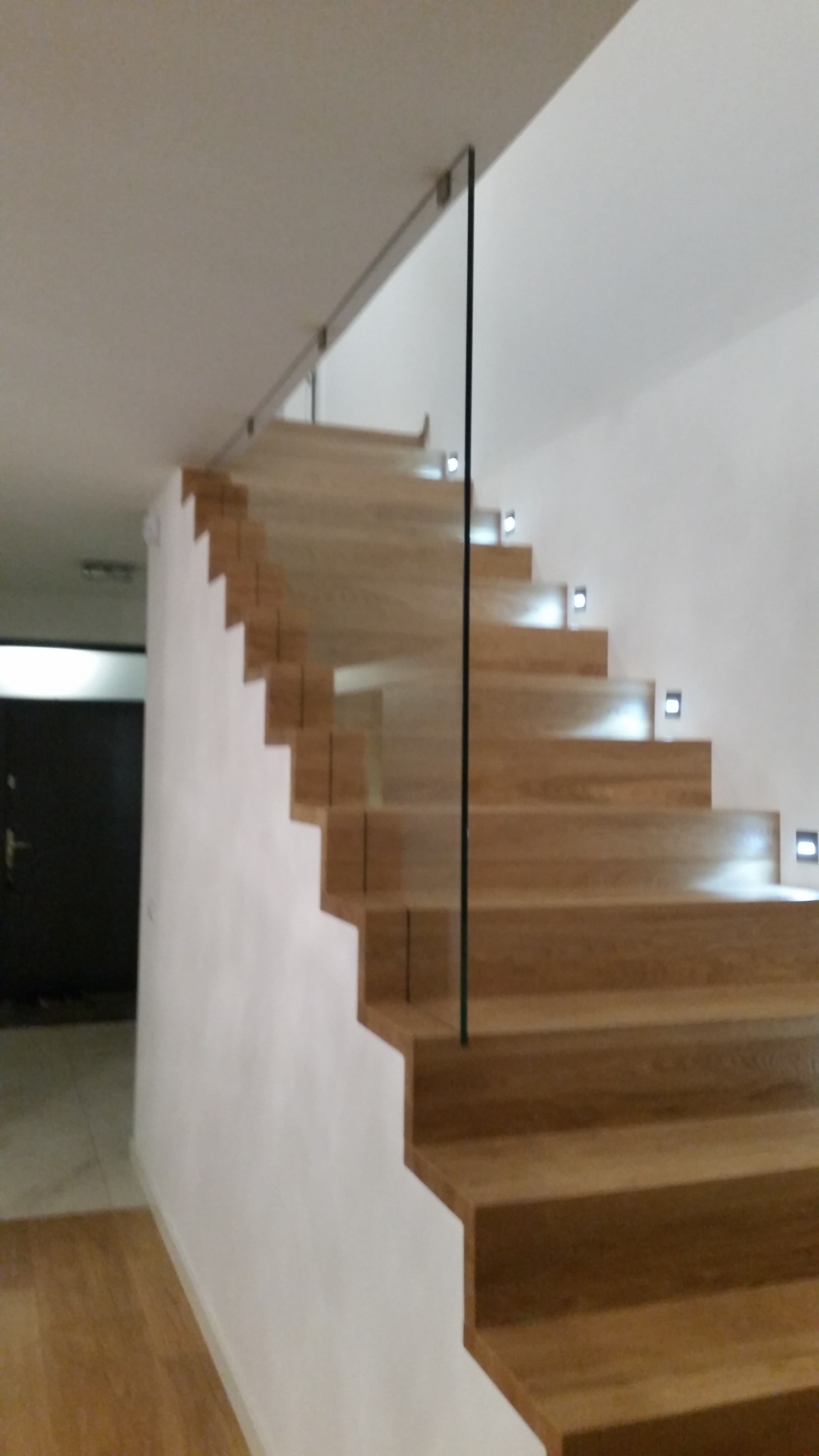 Nowoczesne schody drewniane z podświetleniem LED i szklaną taflą zabezpieczającą, widok z dołu.