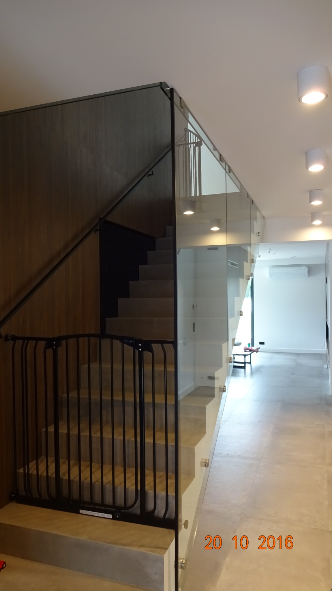 Nowoczesne schody z przeszkloną balustradą w Sokołowie Podlaskim, zabezpieczone czarną barierką dla dzieci, widoczne elementy montażowe szkła.