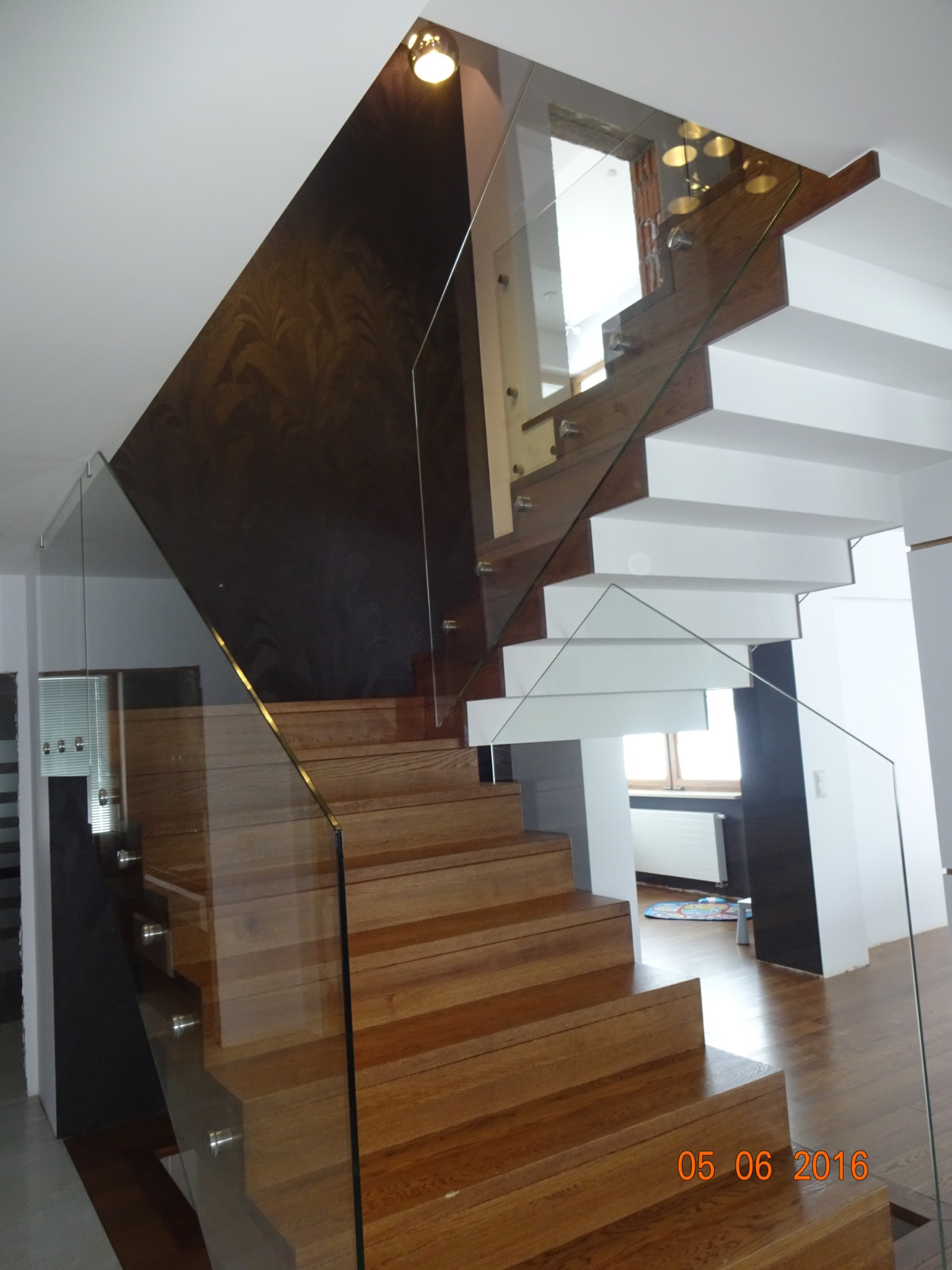 Nowoczesne schody drewniane z balustradą ze szkła hartowanego, widok z dołu, oświetlenie punktowe.