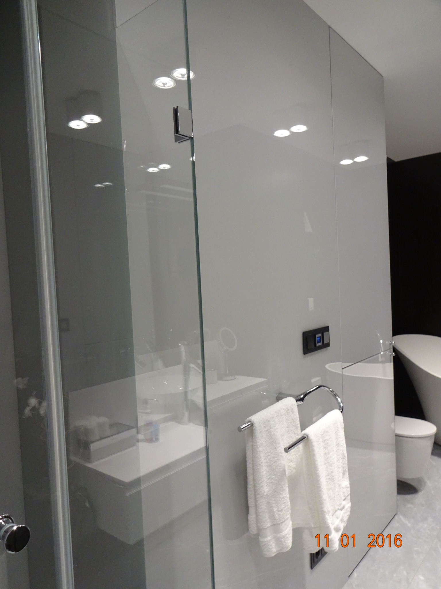 Nowoczesna łazienka z kabiną prysznicową ze szkła hartowanego, widoczny fragment umywalki, toaleta i wanna wolnostojąca, białe ręczniki na chromowanym wieszaku.