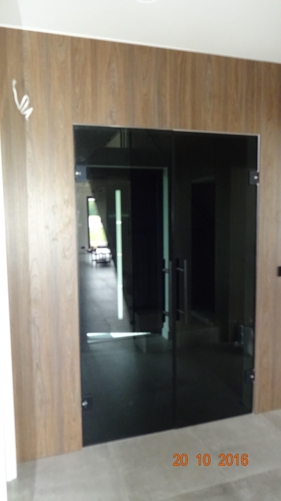 Ciemne, szklane drzwi wewnętrzne z metalowymi uchwytami, osadzone w drewnopodobnej okleinie, widok na jasne pomieszczenie w głębi.