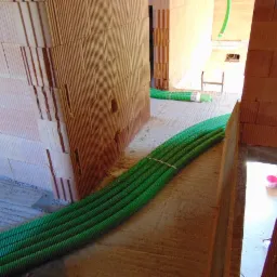 Wiązka zielonych rur wentylacyjnych leżąca na surowym podłożu w budynku w trakcie budowy z czerwonej cegły dziurawki.