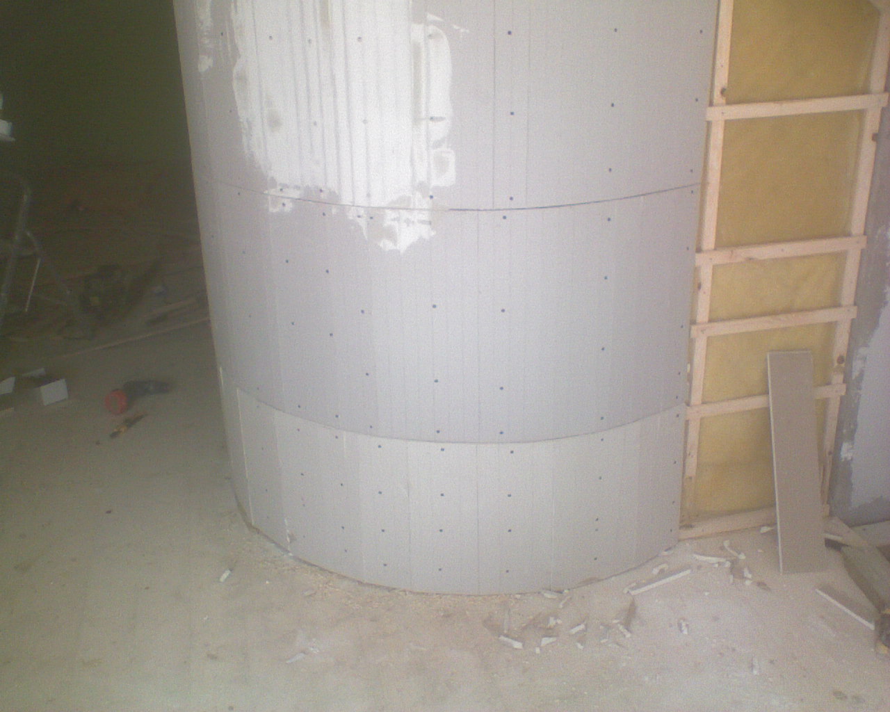 Konstrukcja z płyt gipsowo-kartonowych, ułożonych warstwowo po łuku, przytwierdzonych do ściany z izolacją wełną mineralną, widoczne ślady gładzi i wkręty, na podłodze resztki materiałów.