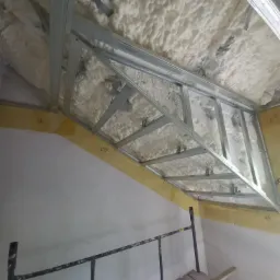 Montaż sufitu podwieszanego z metalową konstrukcją i izolacją z pianki poliuretanowej, widoczny fragment rusztowania.