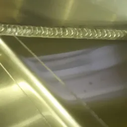 Szczegółowe zbliżenie spawu na metalowej powierzchni z widocznymi śladami po obróbce, jasne oświetlenie podkreśla strukturę spoiny.