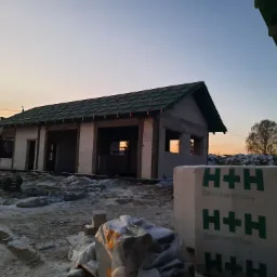 Budowa domu w stanie surowym otwartym o wschodzie słońca, widoczne bloczki betonowe H+H, częściowo ośnieżony teren.
