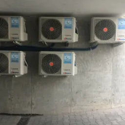 Pięć jednostek zewnętrznych klimatyzacji Electra DC Inverter zamontowanych na szarej, betonowej ścianie, połączonych niebieskim przewodem ochronnym.