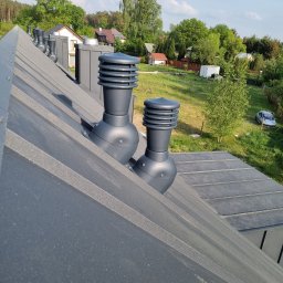 Usługi Ogólnobudowlane - Szary dach z blachy trapezowej z zamontowanymi, nowoczesnymi kominkami wentylacyjnymi. W tle zabudowa jednorodzinna i zieleń.