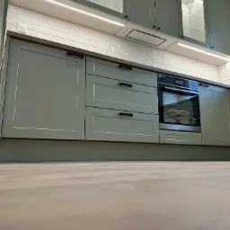 Fragment zabudowy kuchennej w odcieniach zieleni z piekarnikiem Electrolux i oświetleniem LED podszafkowym, widok z poziomu podłogi.