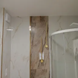 Nowoczesna łazienka z kabiną prysznicową narożną, marmurowymi płytkami i złotymi akcentami: uchwyt na papier toaletowy i wieszak na ręcznik w kolorze złota.