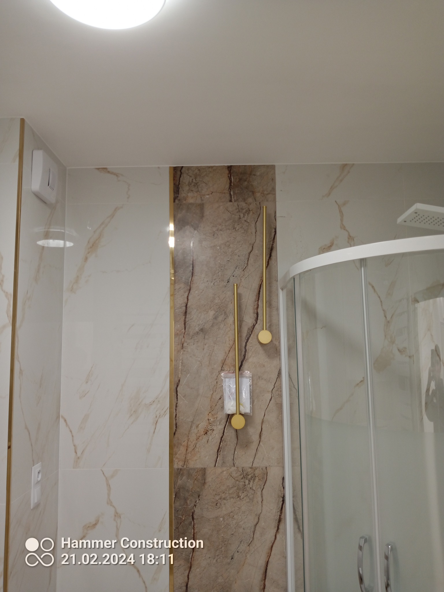 Nowoczesna łazienka z kabiną prysznicową narożną, marmurowymi płytkami i złotymi akcentami: uchwyt na papier toaletowy i wieszak na ręcznik w kolorze złota.