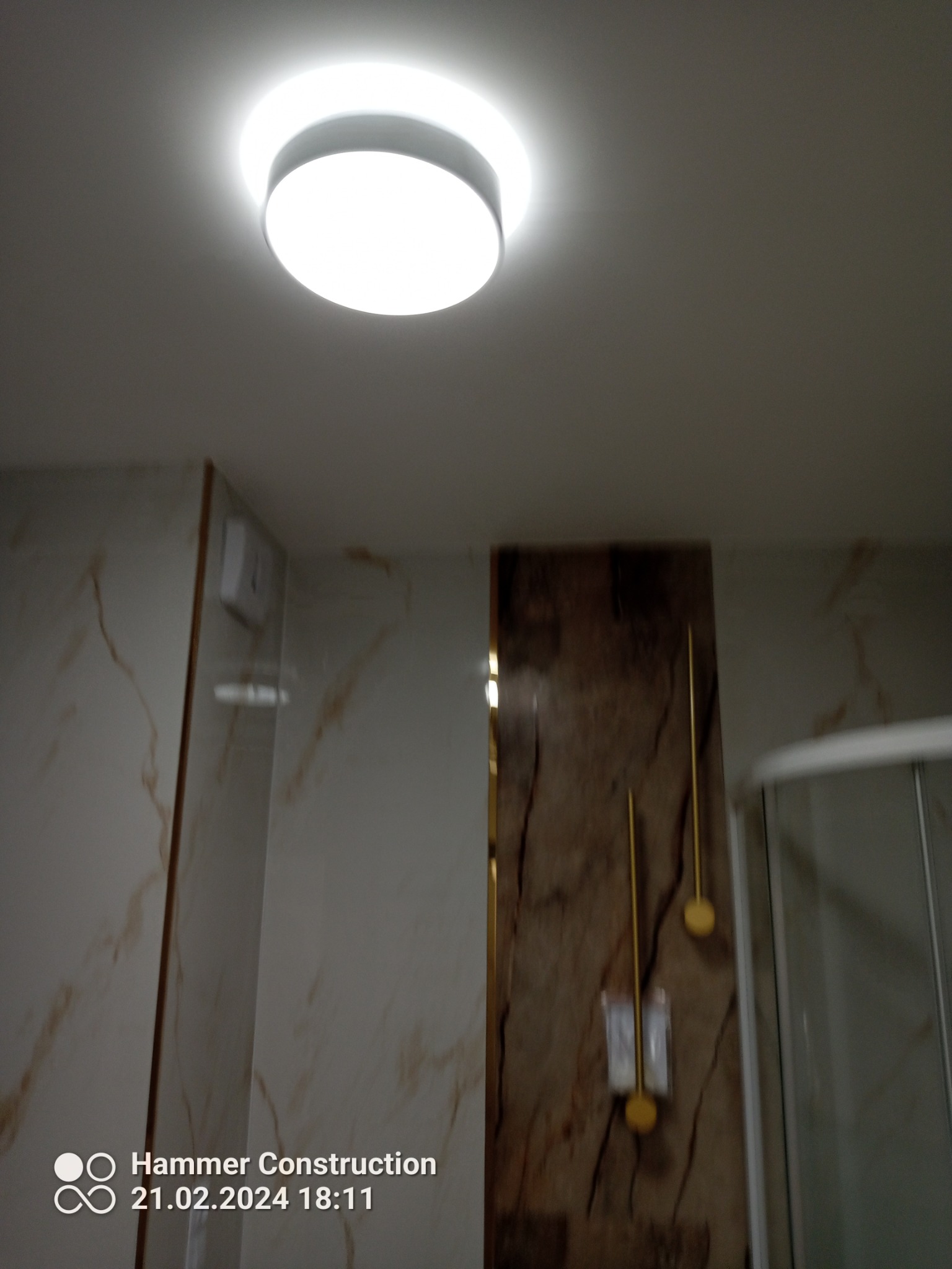 Zamontowana okrągła lampa sufitowa LED w łazience z marmurowymi płytkami i elementami dekoracyjnymi w kolorze złota.