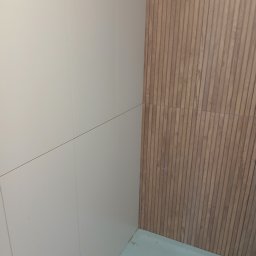 Snowbud Bartosz Śnieżewski - Wykończona ściana z płytek imitujących drewno, sąsiadująca z gładką, jasną ścianą. Widoczny fragment podłogi. Minimalistyczny design.