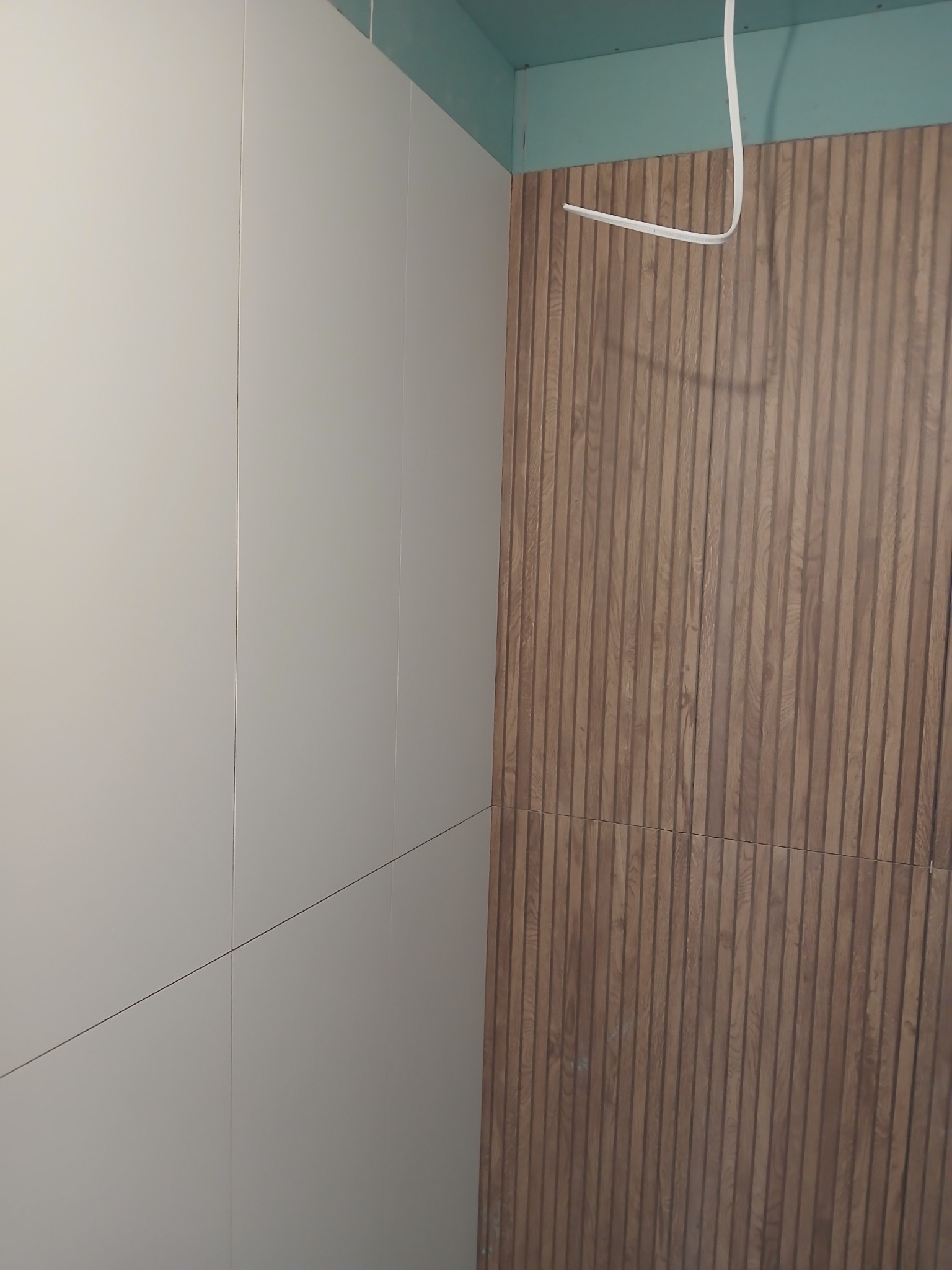 Ściana wykończona płytami w odcieniach bieli i brązu z widoczną instalacją elektryczną pod sufitem, ukazująca nowoczesny design wnętrza.