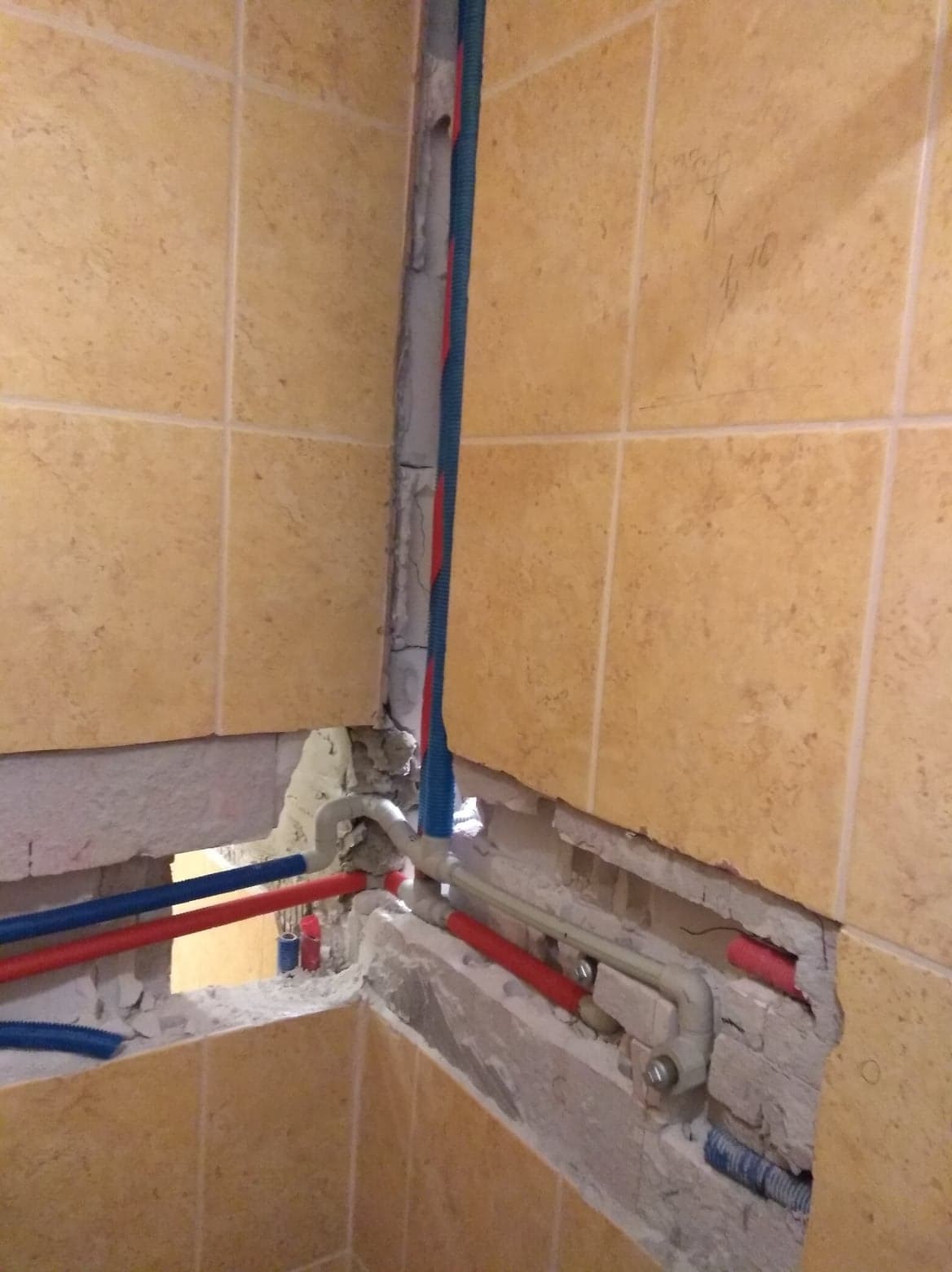 Fragment ściany z widocznymi rurami instalacji wodnej i kanalizacyjnej w trakcie remontu łazienki, z odsłoniętą instalacją w ścianie z beżowych płytek.