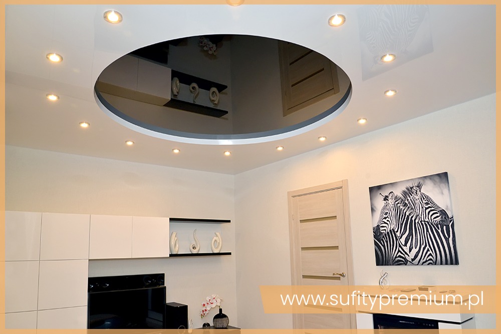 Nowoczesne wnętrze z podwieszanym sufitem z okrągłym, lustrzanym wkładem i punktowym oświetleniem LED, widoczne białe meble i obraz z motywem zebry na ścianie.