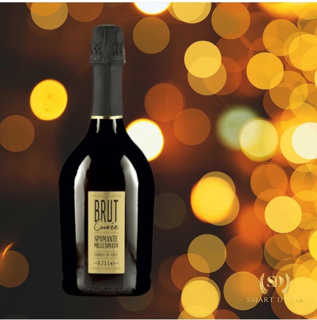 Butelka ciemnego wina musującego Brut Cuvée Millesimato na rozmytym tle z bokeh w odcieniach pomarańczy i żółci.