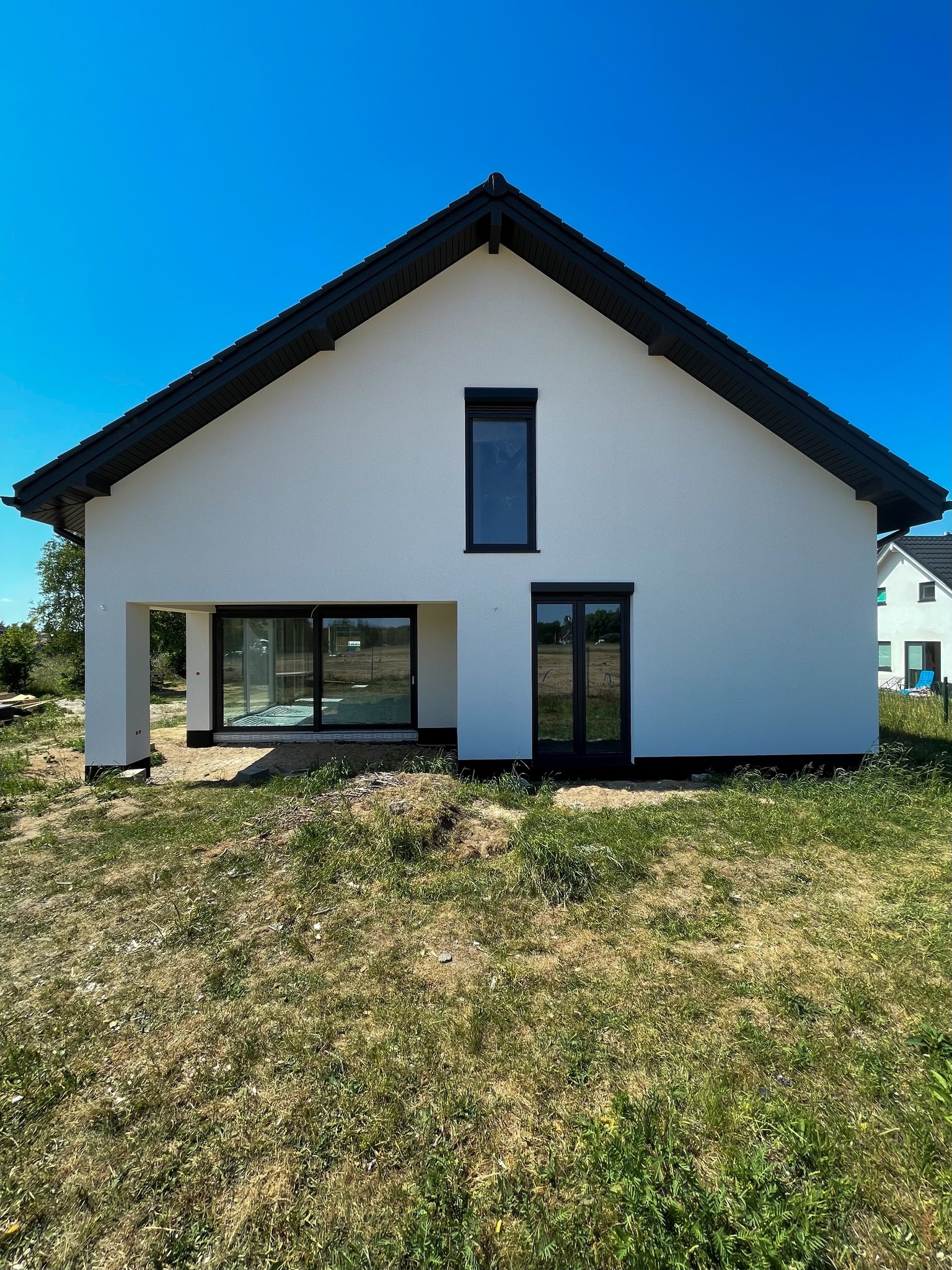 Biały dom w stylu nowoczesnej stodoły z czarnym dachem i stolarką okienną, widoczny z zewnątrz na tle błękitnego nieba.