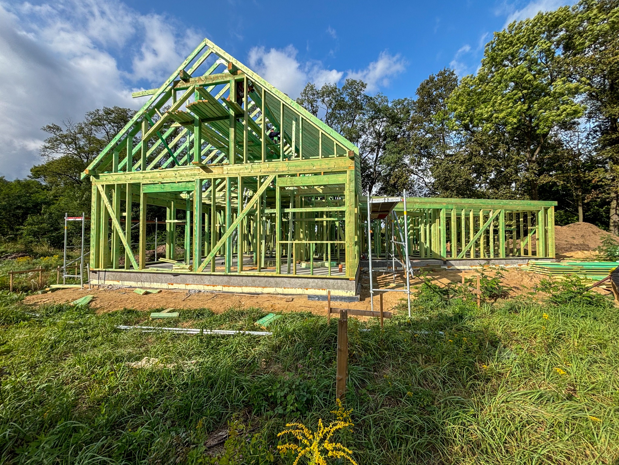 Wznoszenie konstrukcji domu z drewna, widoczny szkielet budynku na tle zieleni i błękitnego nieba.