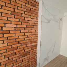 Ceglana ściana dekoracyjna sąsiaduje z marmurową okładziną prysznica, podłoga wyłożona panelami imitującymi drewno.