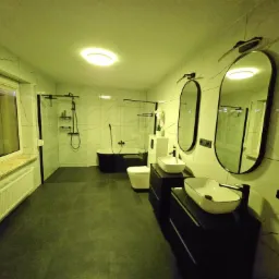 Wykończona łazienka z czarną wanną wolnostojącą, białymi umywalkami nablatowymi na czarnych szafkach i marmurowymi płytkami na ścianach, oświetlona światłem LED.