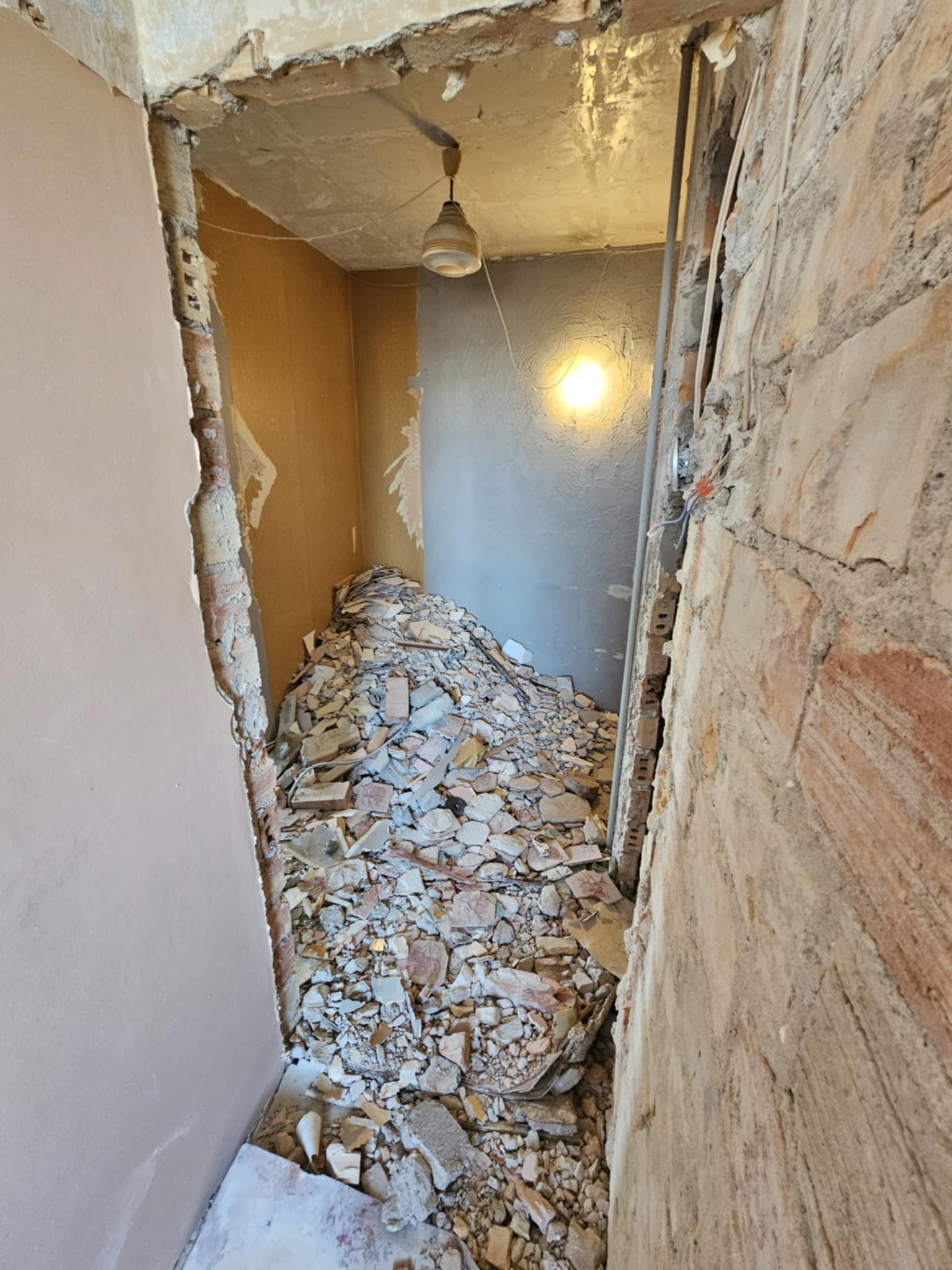 Stare cegły i gruz po demontażu ścian w trakcie remontu, widoczne odsłonięte instalacje elektryczne, surowy stan przed wykończeniem.