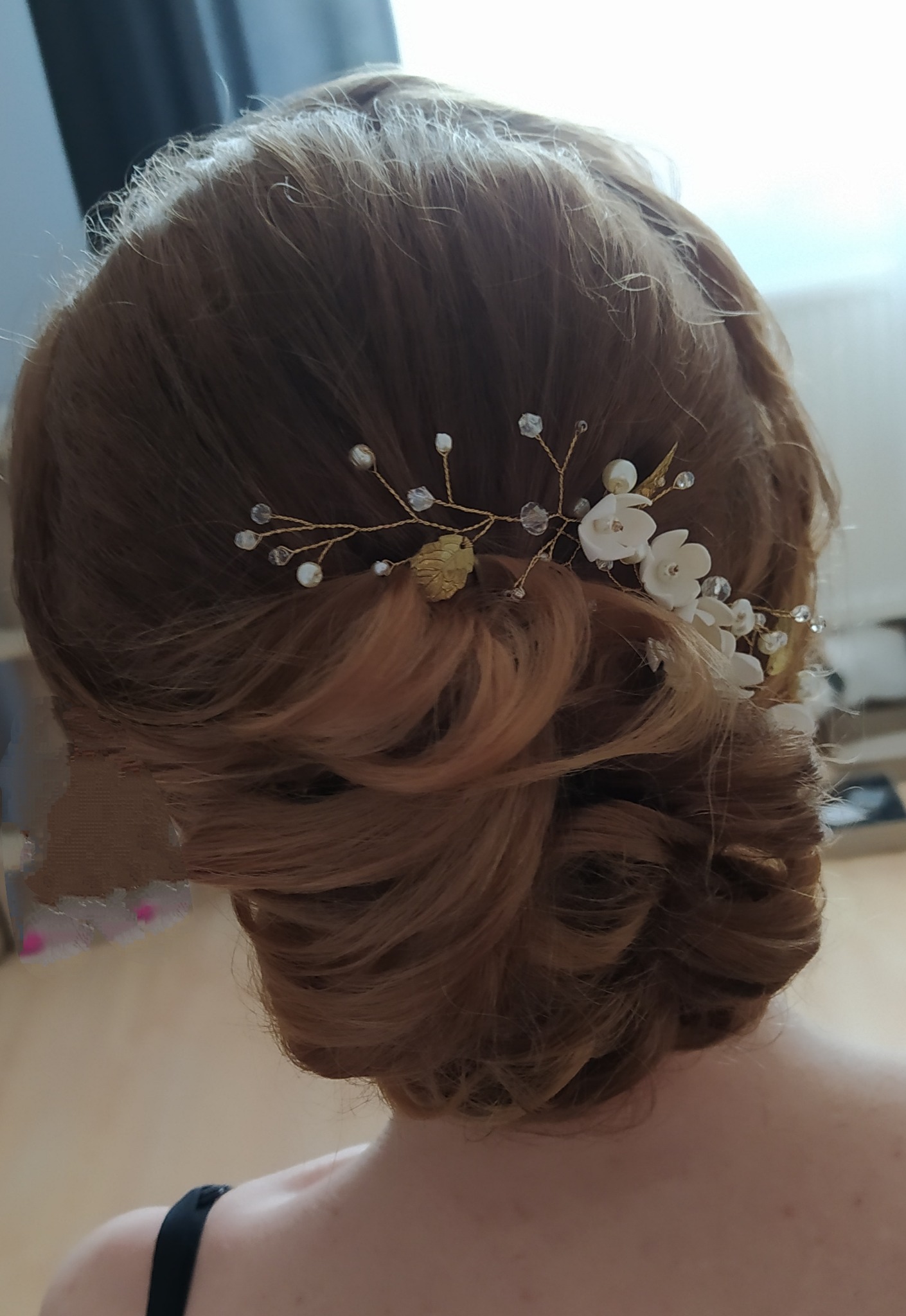 Upięcie włosów w kok z dekoracyjną spinką z białymi kwiatami i złotymi listkami, widok z tyłu, włosy w odcieniu miedzianego blondu.