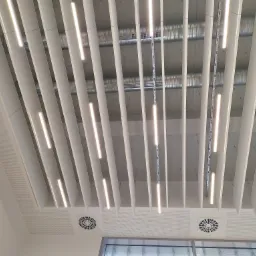 Sufit podwieszany z liniowymi lampami LED, widoczne elementy wentylacji i instalacje pod sufitem.