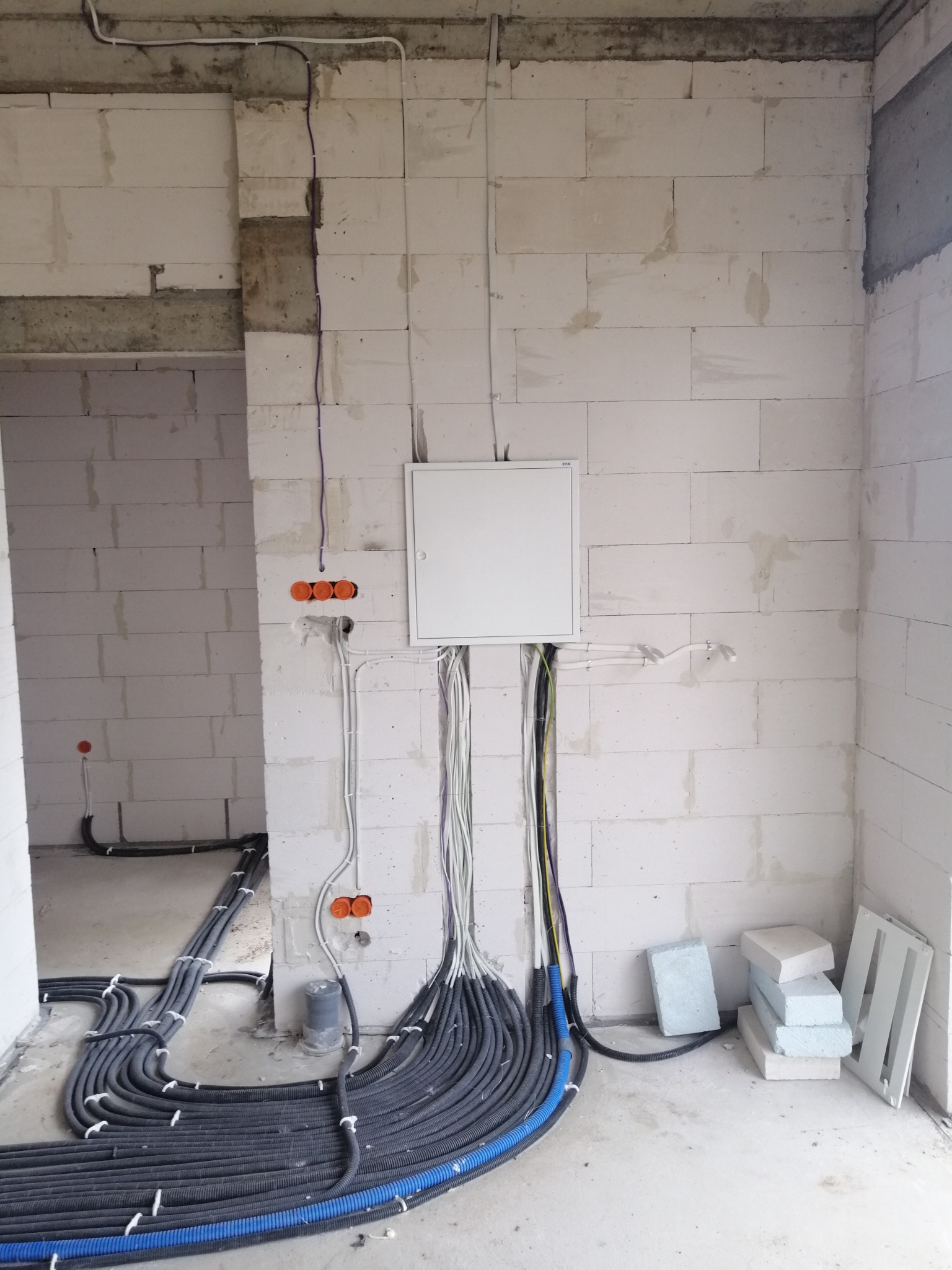 Rozprowadzenie przewodów elektrycznych w peszlach, instalacja w surowym stanie, widoczna skrzynka rozdzielcza i puszki instalacyjne w ścianie z betonu komórkowego.