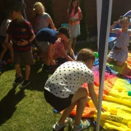 Grupa dzieci bawi się na trawie w kolorowym tunelu z piłeczkami podczas imprezy plenerowej.