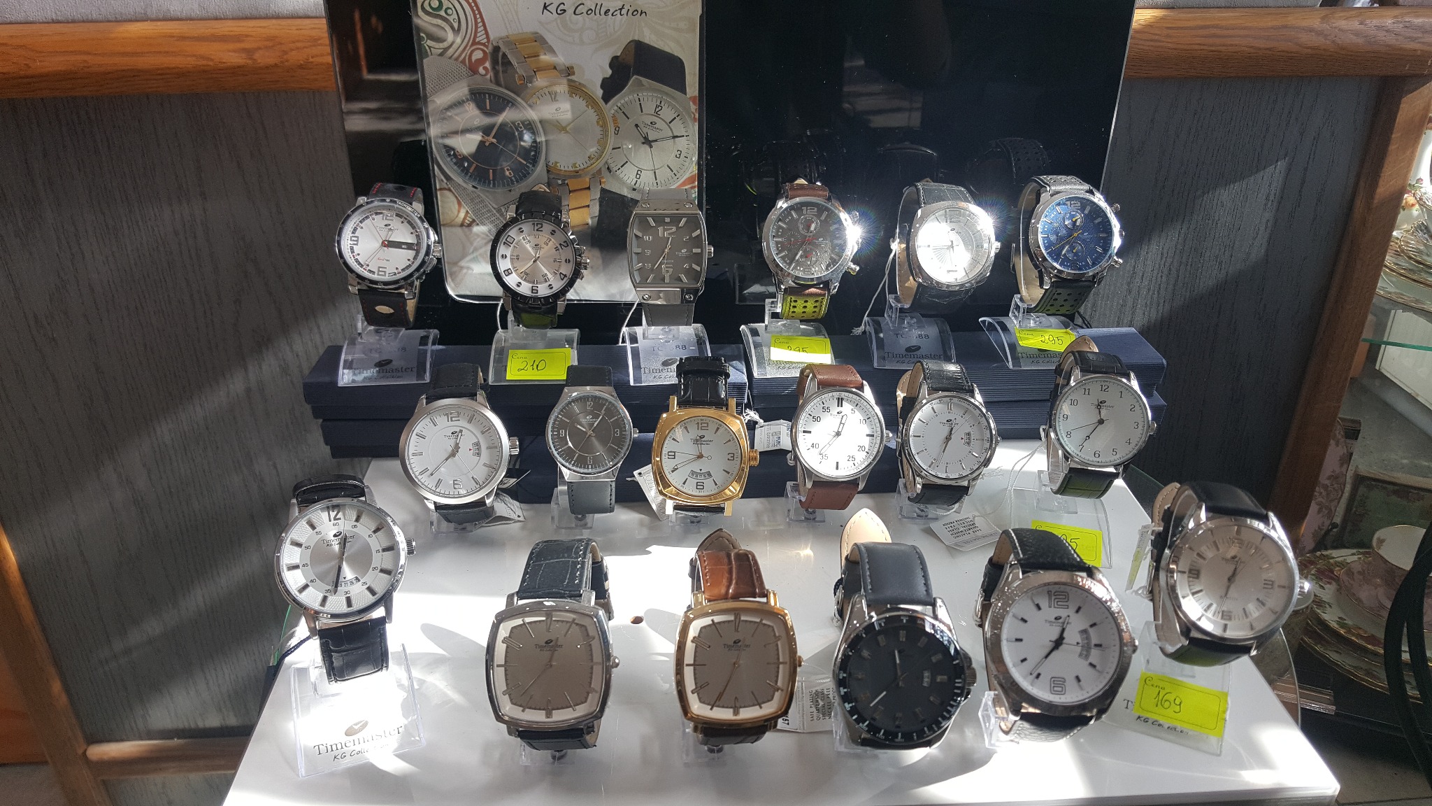 Ekspozycja zegarków marki Timemaster KG Collection z różnymi tarczami i paskami, prezentowana na podwyższeniu z cenami na żółtych etykietach.