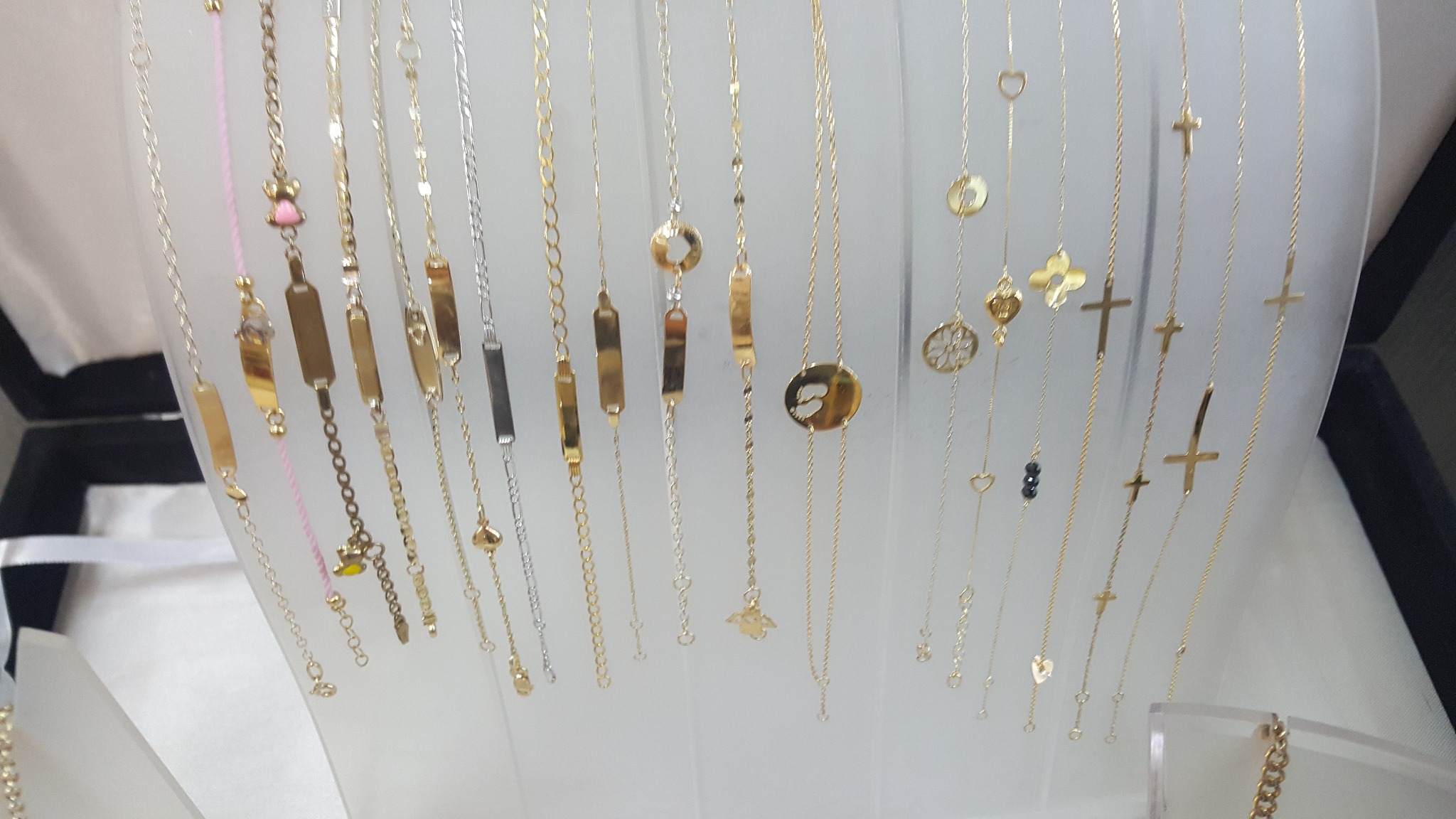 Złote i srebrne łańcuszki z zawieszkami, w tym z motywami krzyżyków, serduszek i blaszek z możliwością graweru, prezentowane na białym tle.