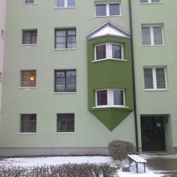 P.H.Krzysztof paludkiewicz - Wielopiętrowy budynek z oknami, pomalowany na jasnozielono, z zielonym wykuszem, na którym widać śnieg. Na dole widać śnieg i ławkę.