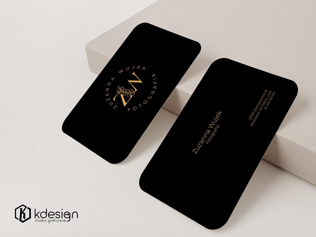 Dwie czarne wizytówki z zaokrąglonymi rogami, złote napisy i logo 'ZW' w okręgu z liśćmi, adres i nazwa 'Zuzanna Wujek Fotografia' na jasnym tle.