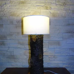 Lampa stołowa z podstawą z naturalnego drewna, z widocznymi słojami i białym abażurem, na tle ściany z dekoracyjnej cegły.