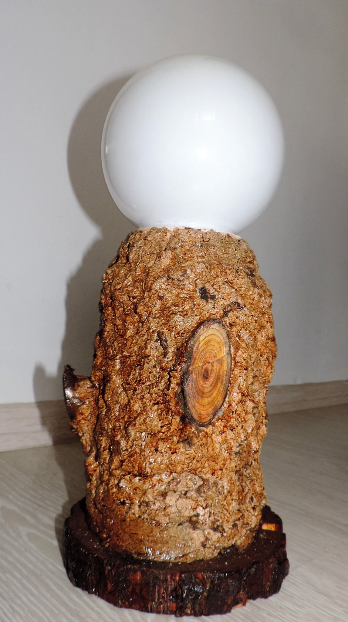 Lampa stołowa z podstawą z kory drzewnej i białą kulą jako klosz.