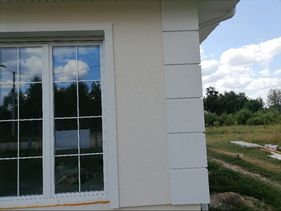 Fragment otynkowanej elewacji domu z oknem, widoczne detale wykończenia i faktura tynku.