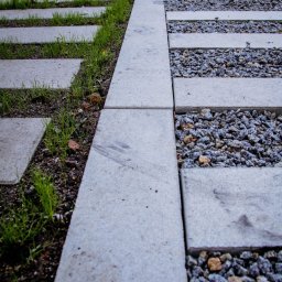 KA Kobierska Pracownia Projektowa - Nawierzchnia z betonowych płyt oddzielonych pasami ziemi z młodą trawą i grysu, tworząca nowoczesny wzór w ogrodzie.
