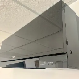 Czarny, błyszczący klimatyzator Mitsubishi Electric Kirigamine Zen zamontowany na białej ścianie pod sufitem kasetonowym.