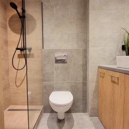 STIM-BUD SP. Z.O.O - Nowoczesna łazienka z kabiną prysznicową typu walk-in, toaletą podwieszaną i szafką pod umywalką w odcieniach szarości i drewna. Minimalistyczny design, płytki wielkoformatowe.