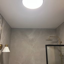 STIM-BUD SP. Z.O.O - Wykończona łazienka z marmurowymi płytkami, złotą armaturą i oświetleniem. Kabina prysznicowa z czarną ramą. Minimalistyczny design, nowoczesne wykończenie.