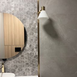STIM-BUD SP. Z.O.O - Nowoczesna łazienka: szare płytki z geometrycznym wzorem, okrągłe lustro z drewnianą szafką, złota lampa ścienna i armatura. Minimalistyczny design.
