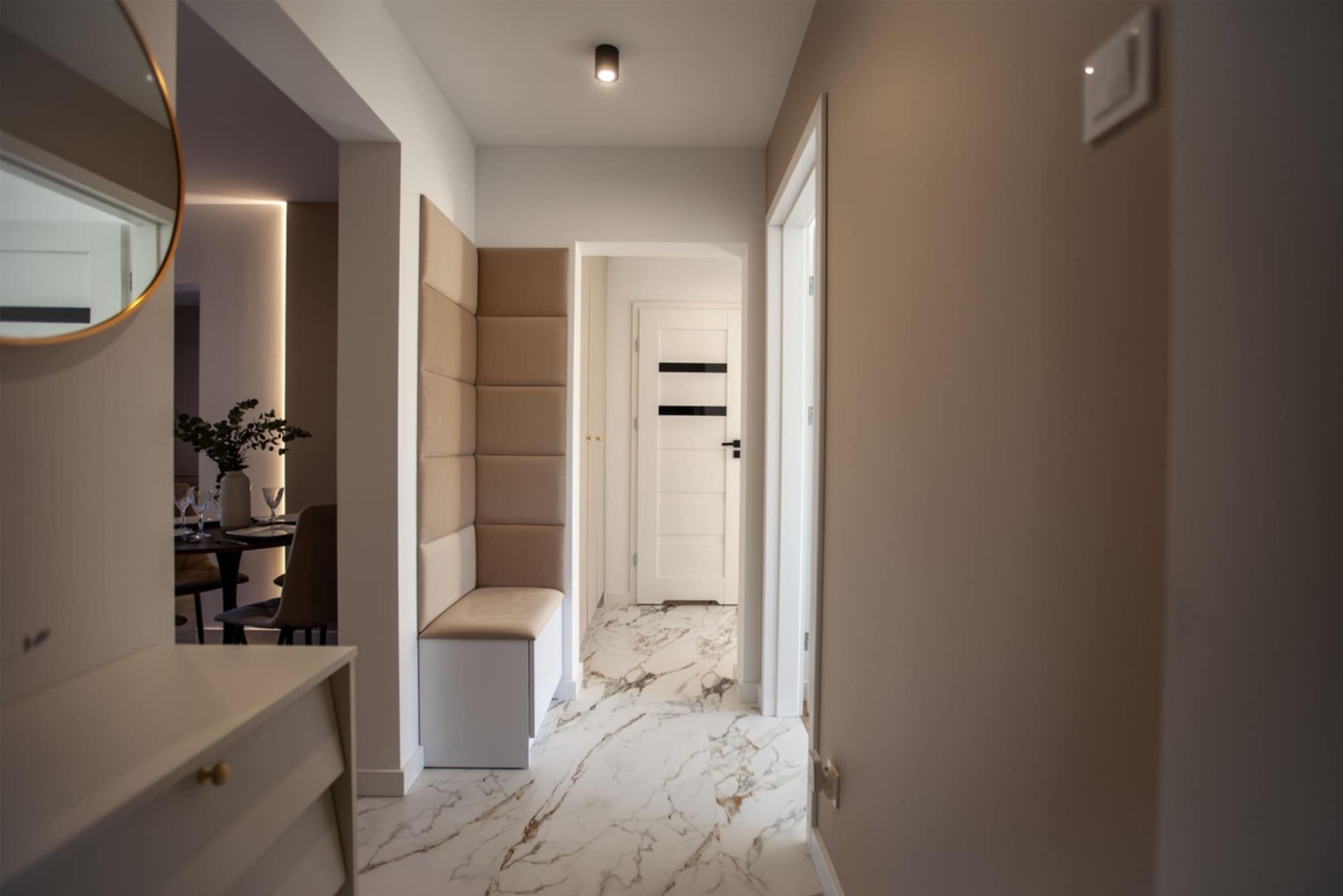 Nowoczesny przedpokój z siedziskiem w zabudowie, podświetleniem i marmurową posadzką. Widok na jadalnię w głębi.