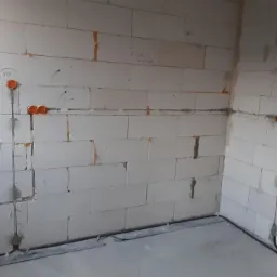 Wewnętrzna instalacja elektryczna w surowym budynku: przewody w ścianach z betonu kom&oacute;rkowego, pomarańczowe puszki instalacyjne, widoczne napisy na ścianie.