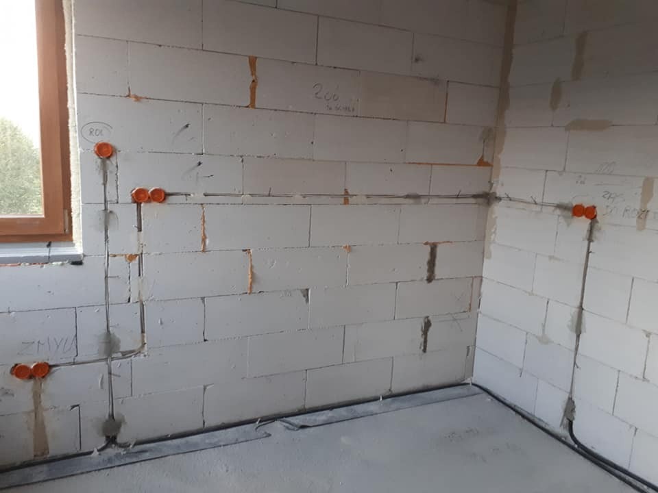 Wewnętrzna instalacja elektryczna w surowym budynku: przewody w ścianach z betonu komórkowego, pomarańczowe puszki instalacyjne, widoczne napisy na ścianie.