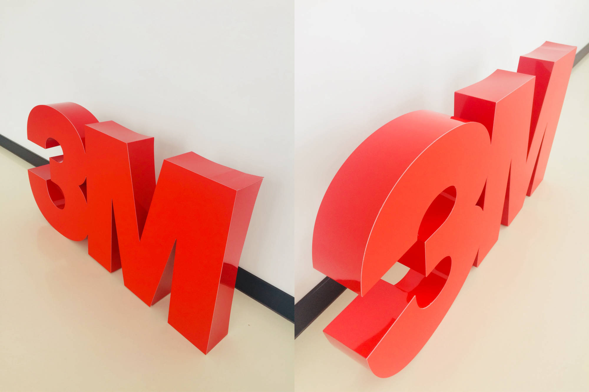 Czerwone, przestrzenne litery 3M zamontowane na styku białej ściany i beżowej podłogi, widoczne z dwóch różnych perspektyw w jednym ujęciu.